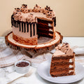 Chocolate cake with a slice on a plate, surrounded by chocolate chips and a fork on a marble surface.