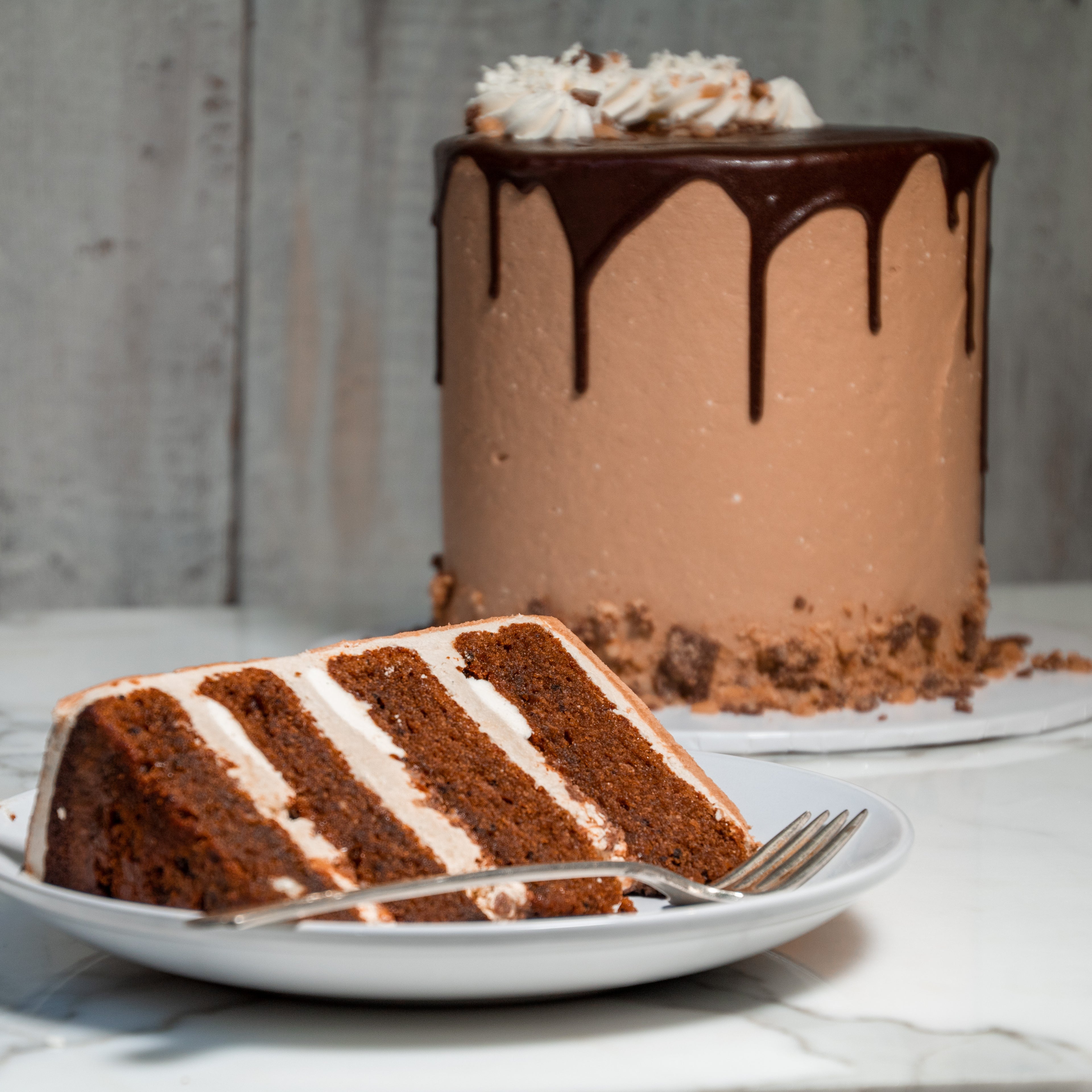 Chocolate cake with a slice cut out, showing layers, on a white plate with a fork.