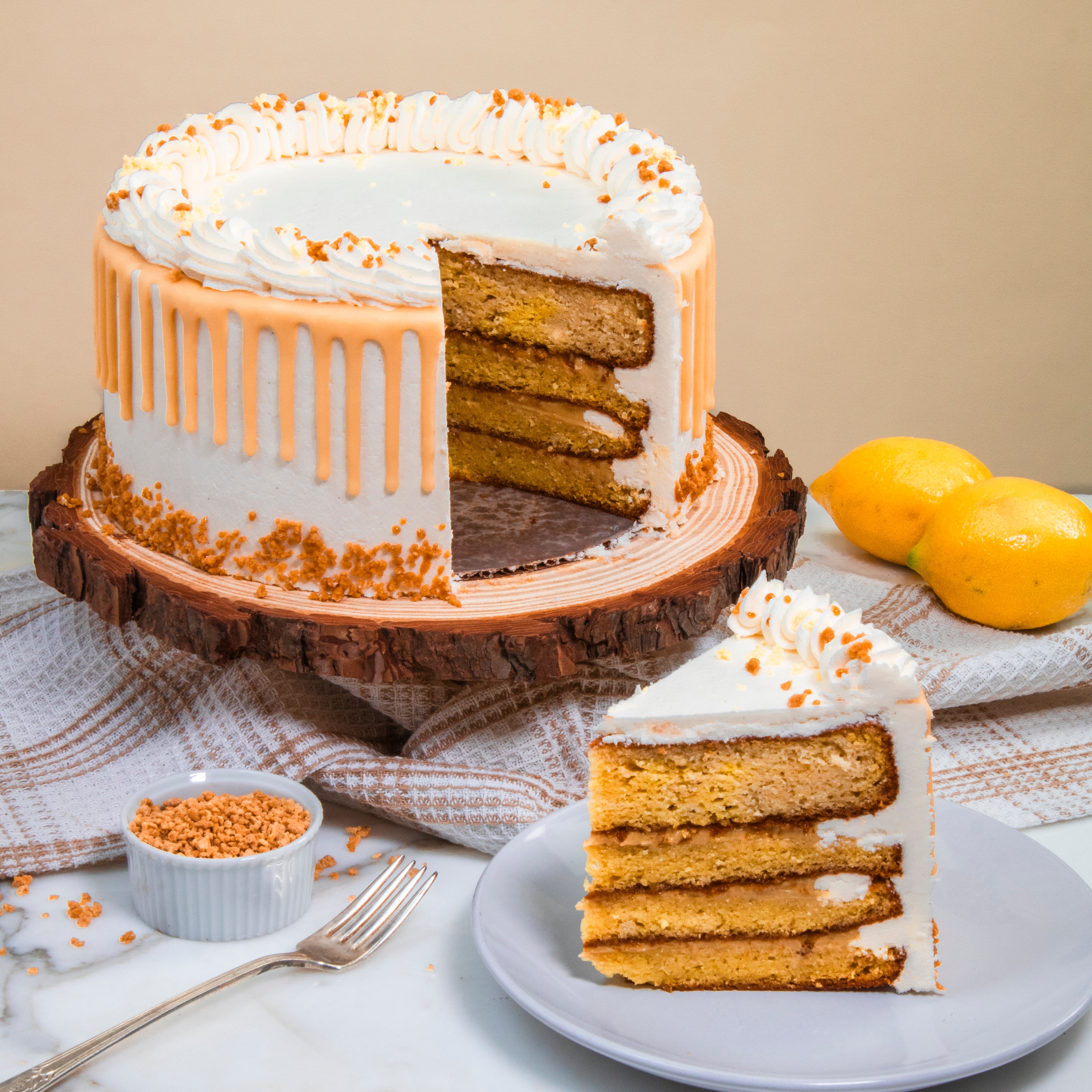 Layered cake with white frosting and orange drizzle on a wooden stand, with a slice on a plate.